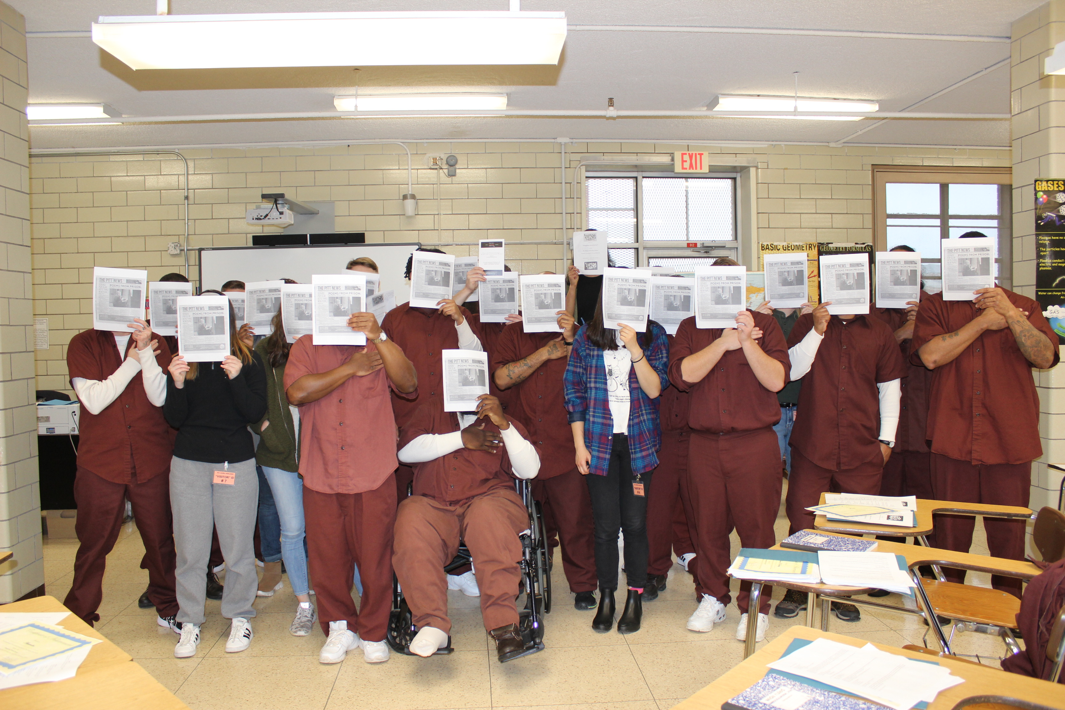 A group of Pitt and incarcerated students stand with articles in front of their faces.